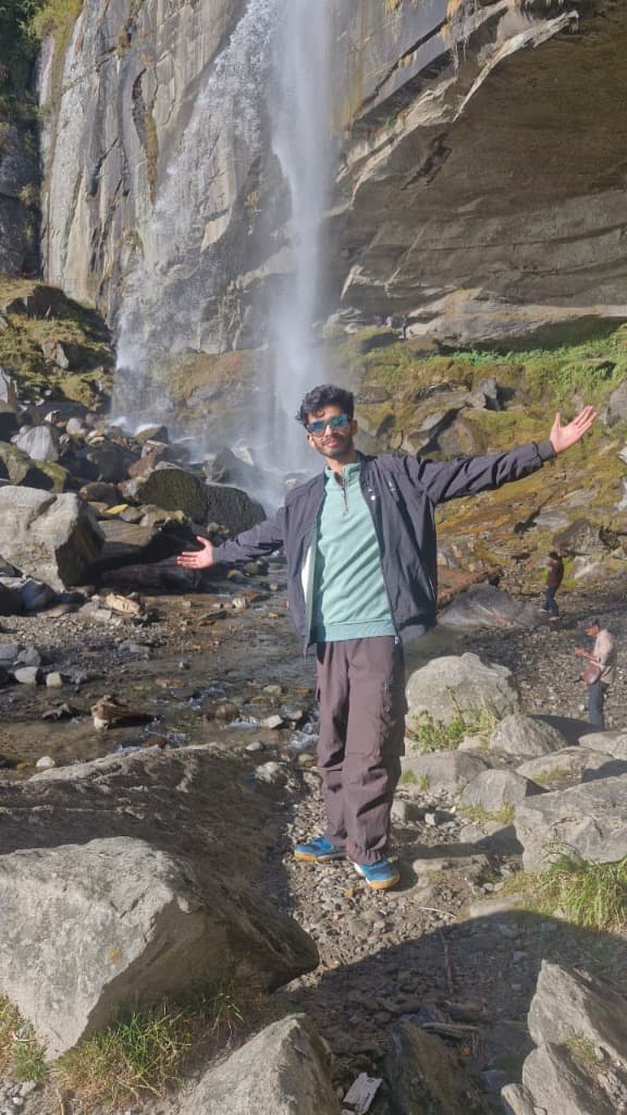 Bipul Chamoli in front of a mountain waterfall, arms stretched wide